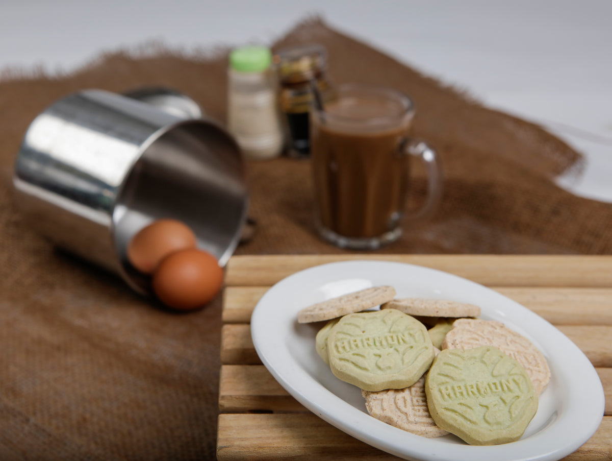 A plate of Harmony cookies beside kopi and two eggs